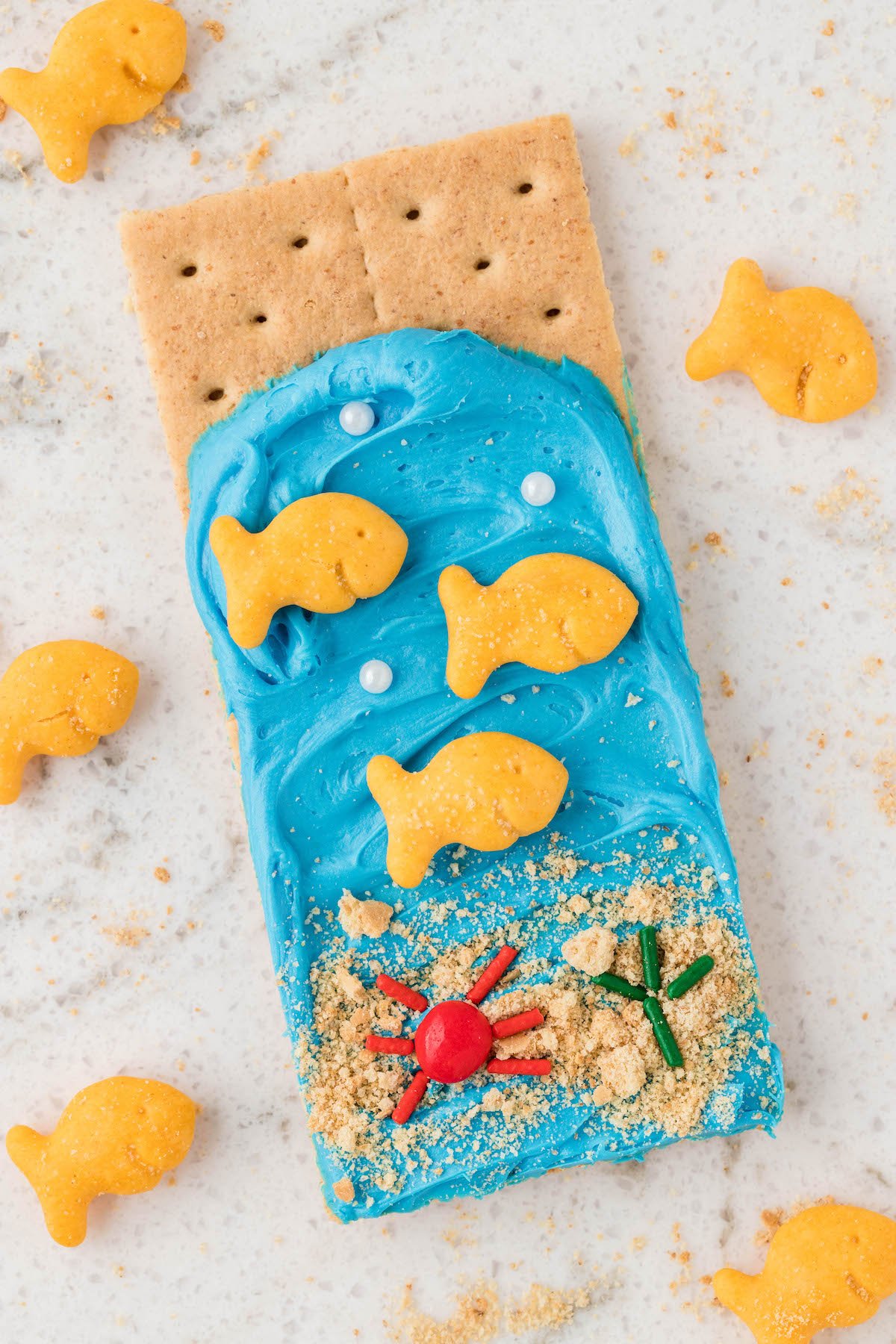 ocean graham cracker with blue frosting, fish crackers and sprinkles.