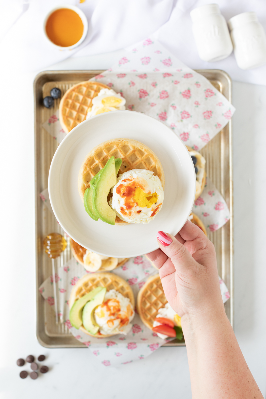 poached eggs on waffles with avocado slices and hot sauce.