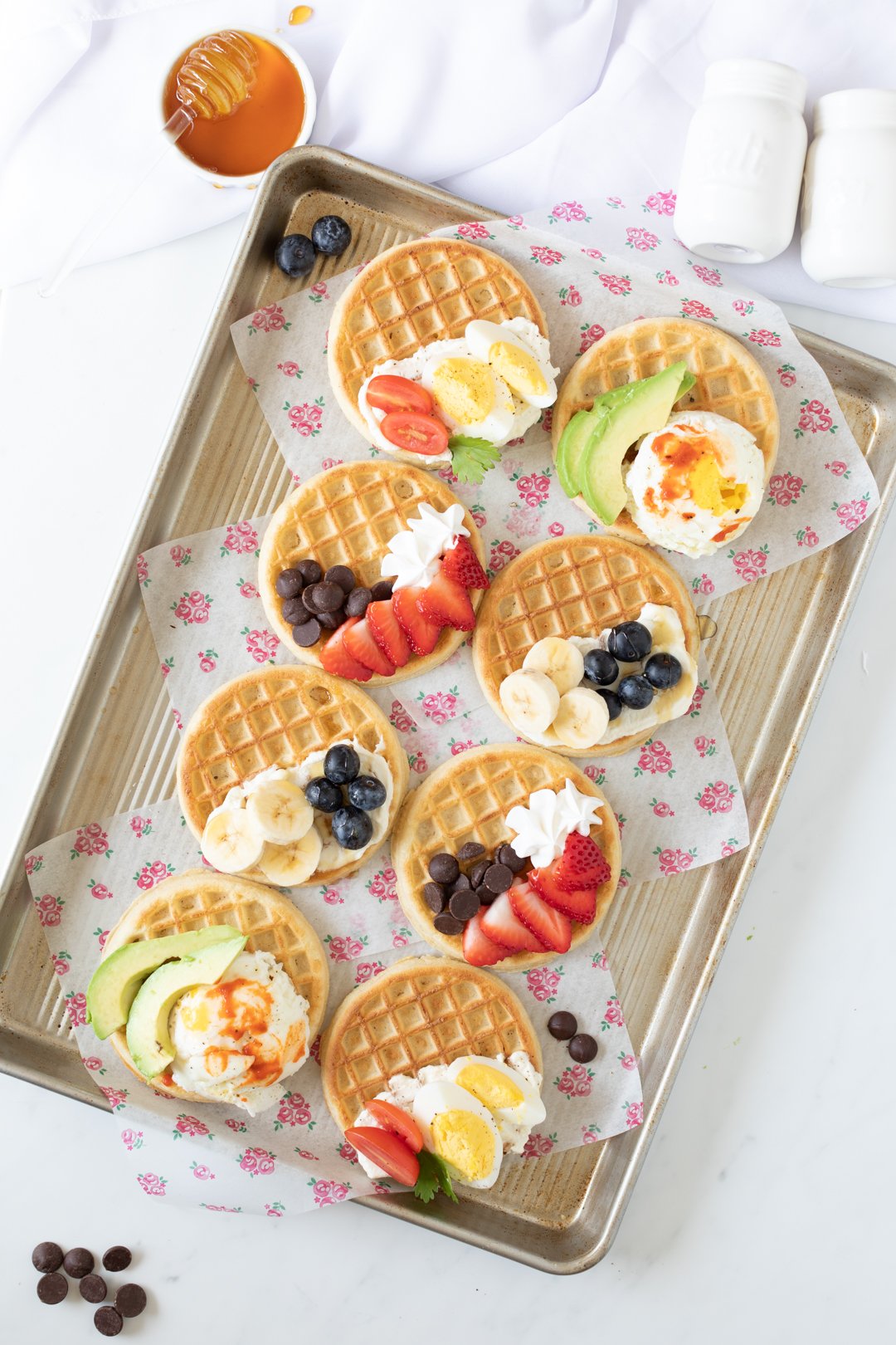 tray of sweet and savory waffles with fresh fruit, poached eggs, veggies, ricotta