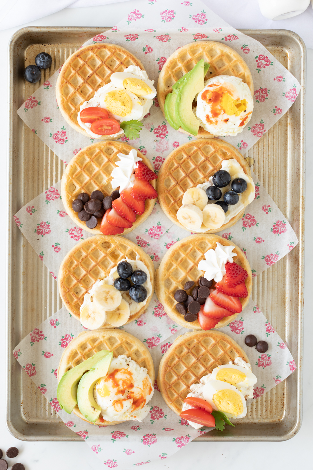 up close baking tray with prepared waffles with a variety of sweet and savory toppings from fresh fruit to poached eggs.