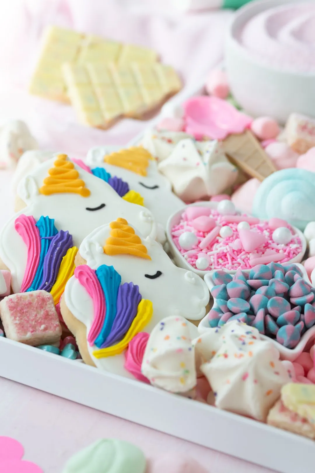 angled view of unicorn hot cocoa board with unicorn cookies, pink sprinkles, birthday meringues