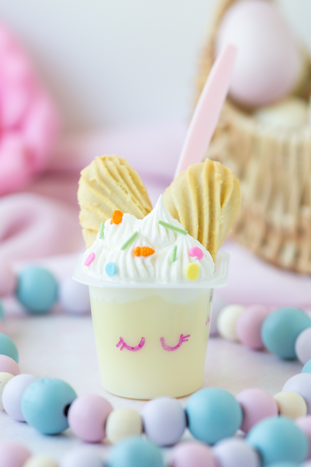 pretty easter pudding cups set on a pastel table with pastel wooden bead garland and easter basket in background