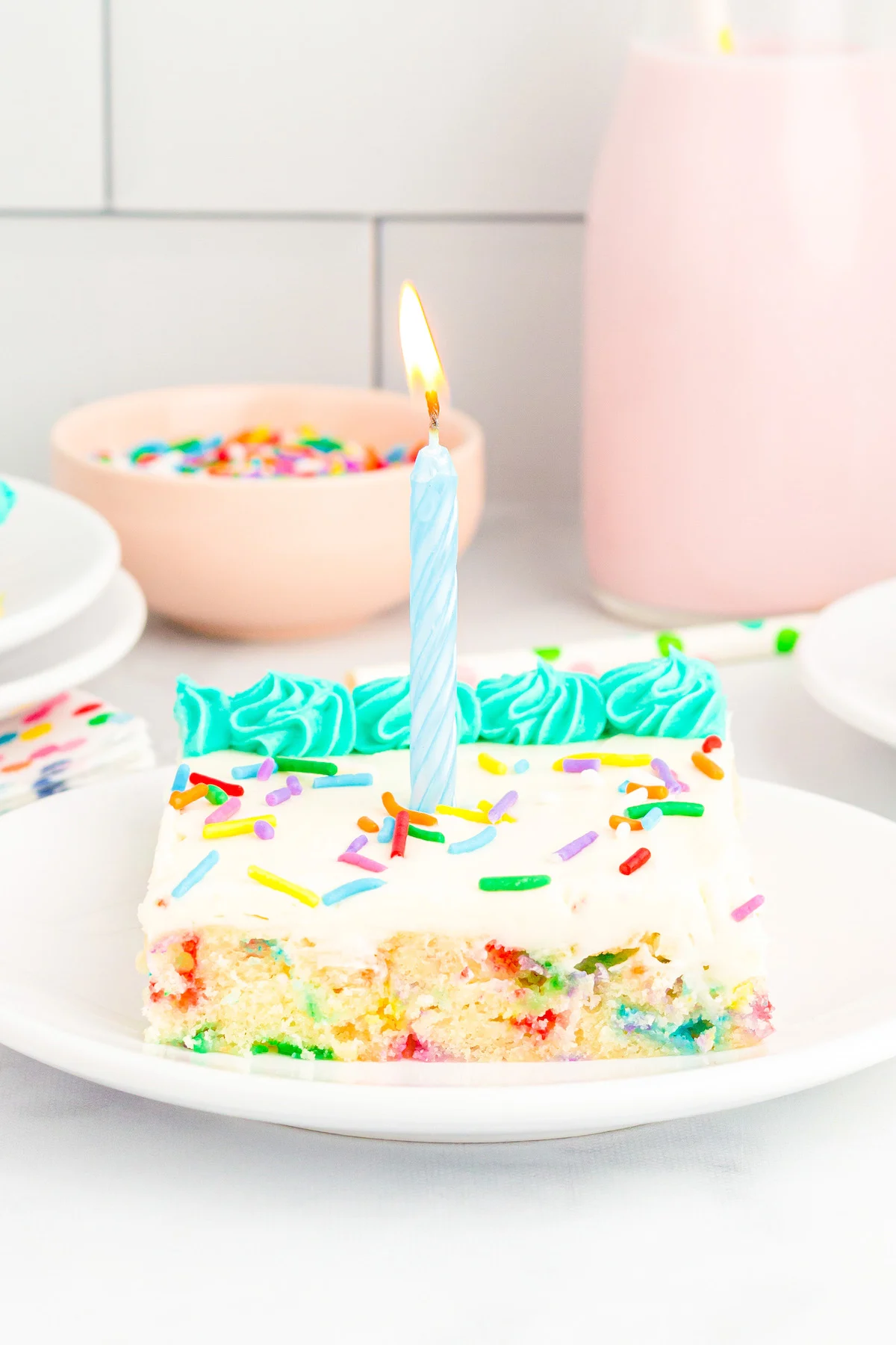 up close photo of a slice of funfetti sheet cake with a lit birthday candle on topl