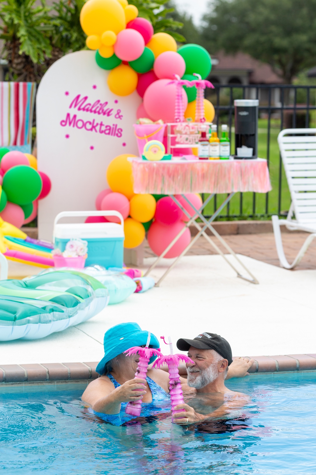 couple inside of a pool cheering with pink palm sippers