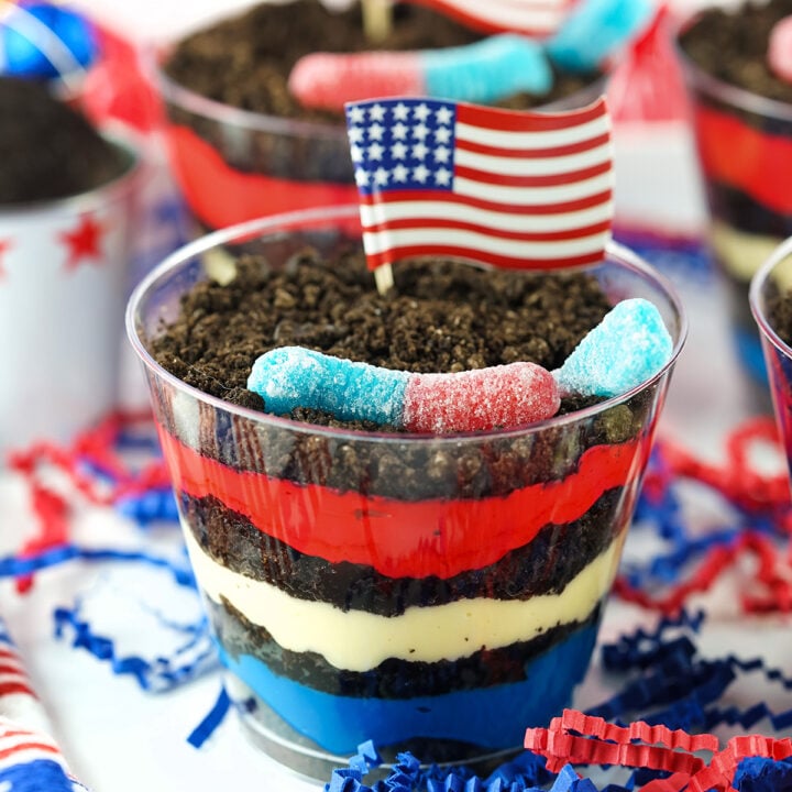 up close view of red, white and blue dirt pudding cups on a tray with american flag cupcake toppers and gummy worms