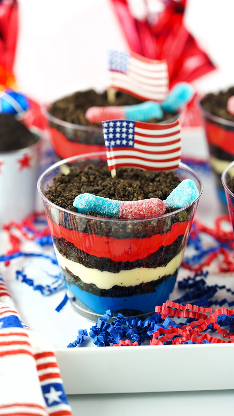 up close view of red, white and blue dirt pudding cups on a tray with american flag cupcake toppers and gummy worms