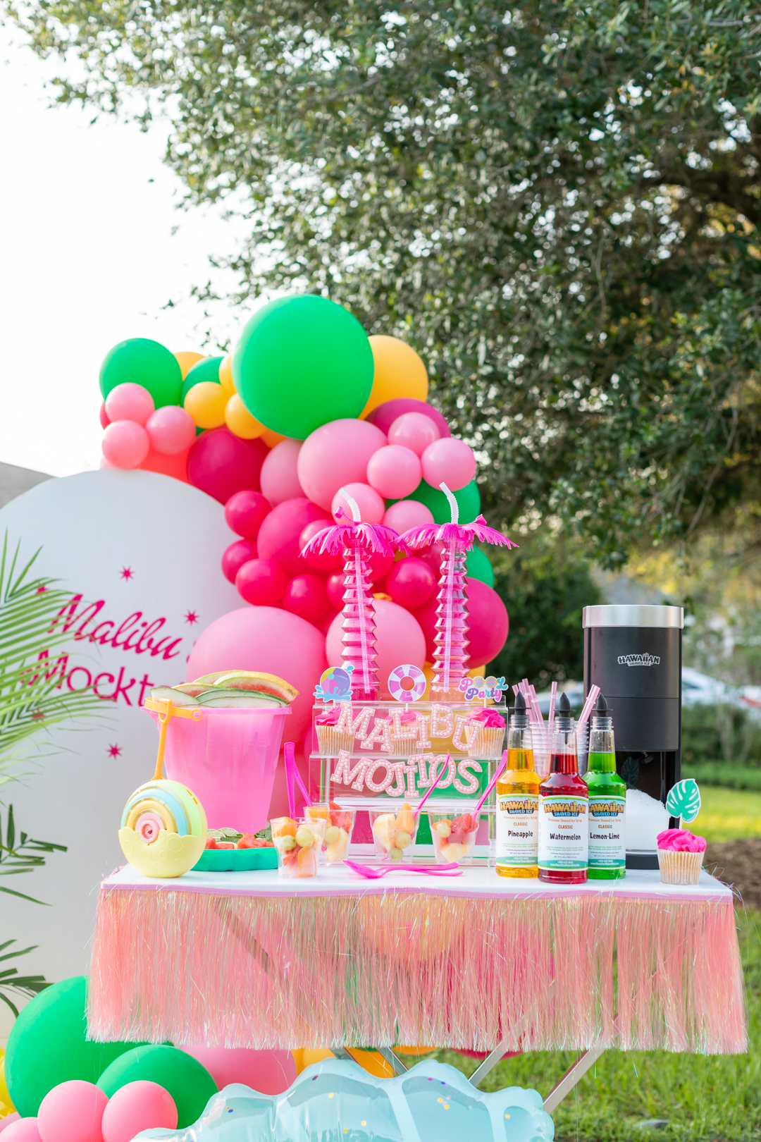 malibu inspired party table with hawaiian shaved ice machine and syrups, gorgeous barbie inspired balloons in background.