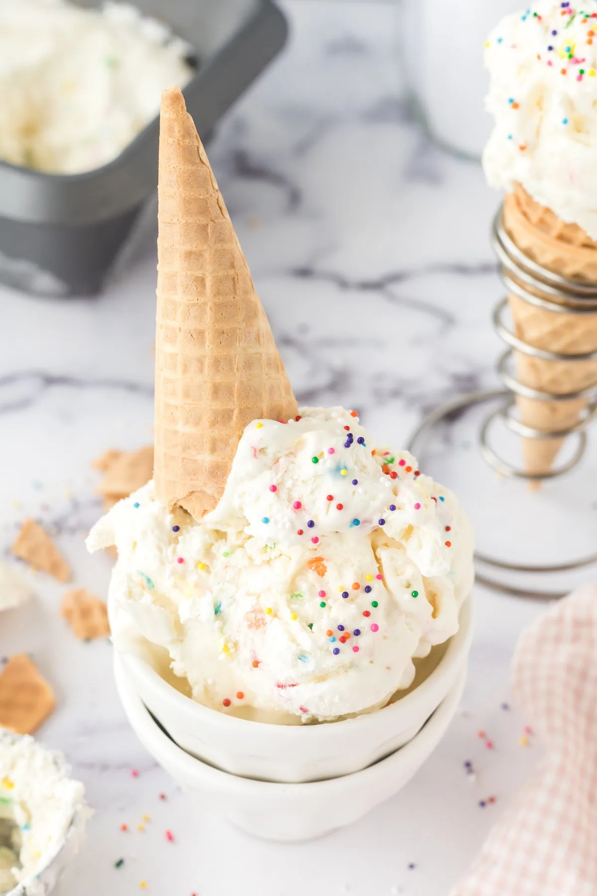 angled down photo of funfetti ice cream in a bowl with a sugar cone set on top.