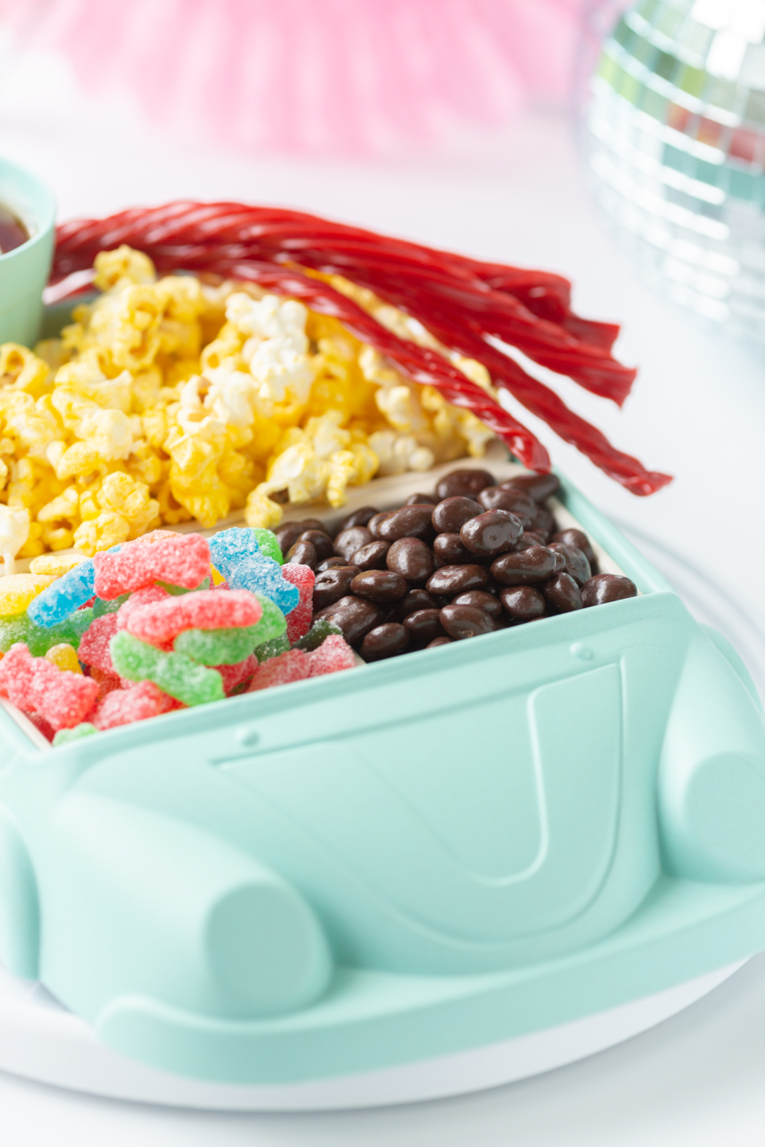side view of a cute car shaped snack tray filled with popcorn and classic movie theater snacks.