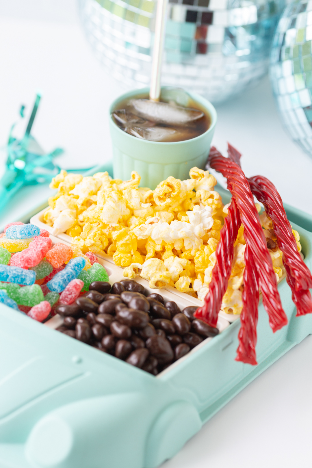 angled shot of classic movie night snacks served in a car-shaped tray. twizzlers, sour patch kids, popcorn, root beer.