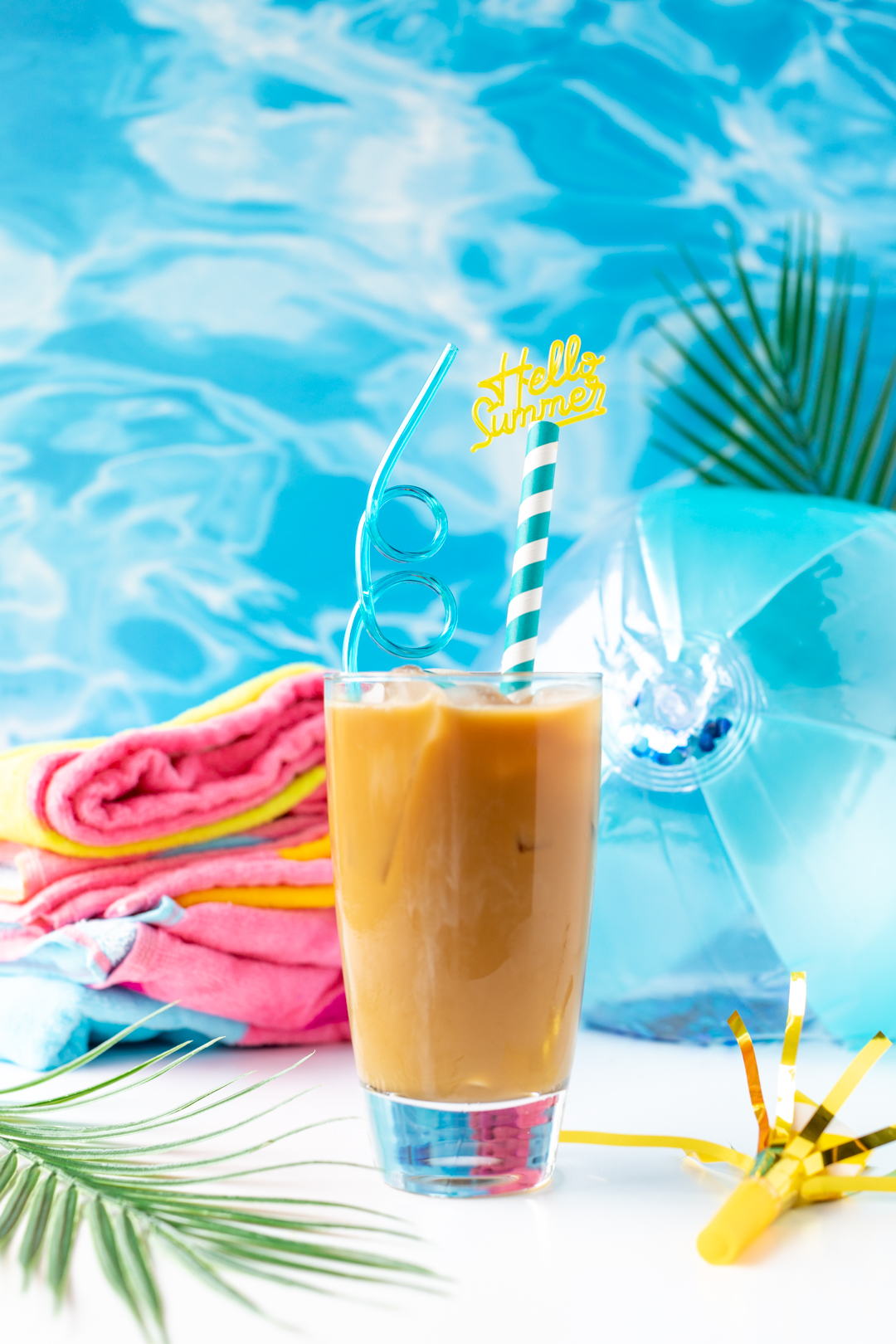 summer iced coffee with hello summer straw, towel and beach ball.