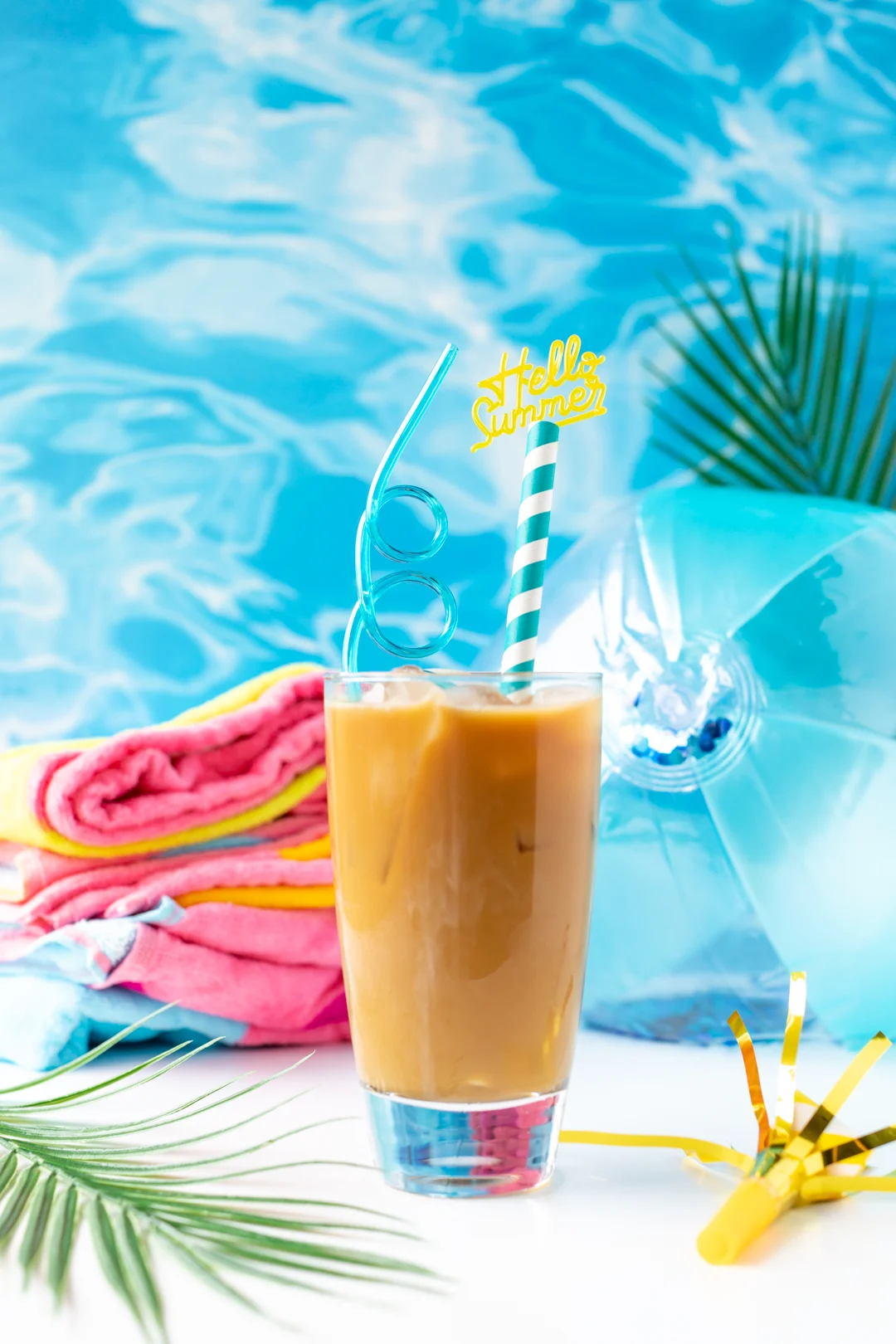 summer iced coffee with hello summer straw, towel and beach ball.