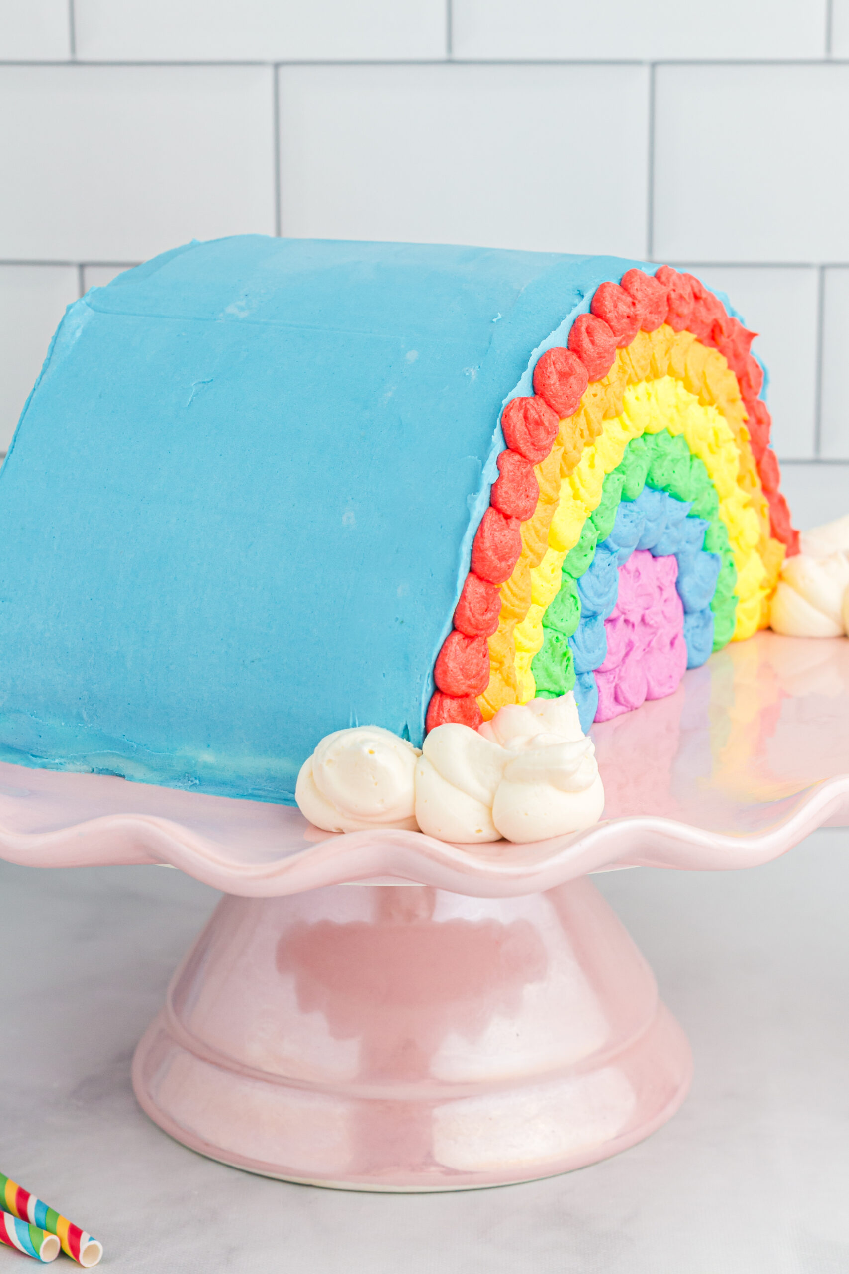 side view of pretty rainbow decorated cake on a pink cake stand.