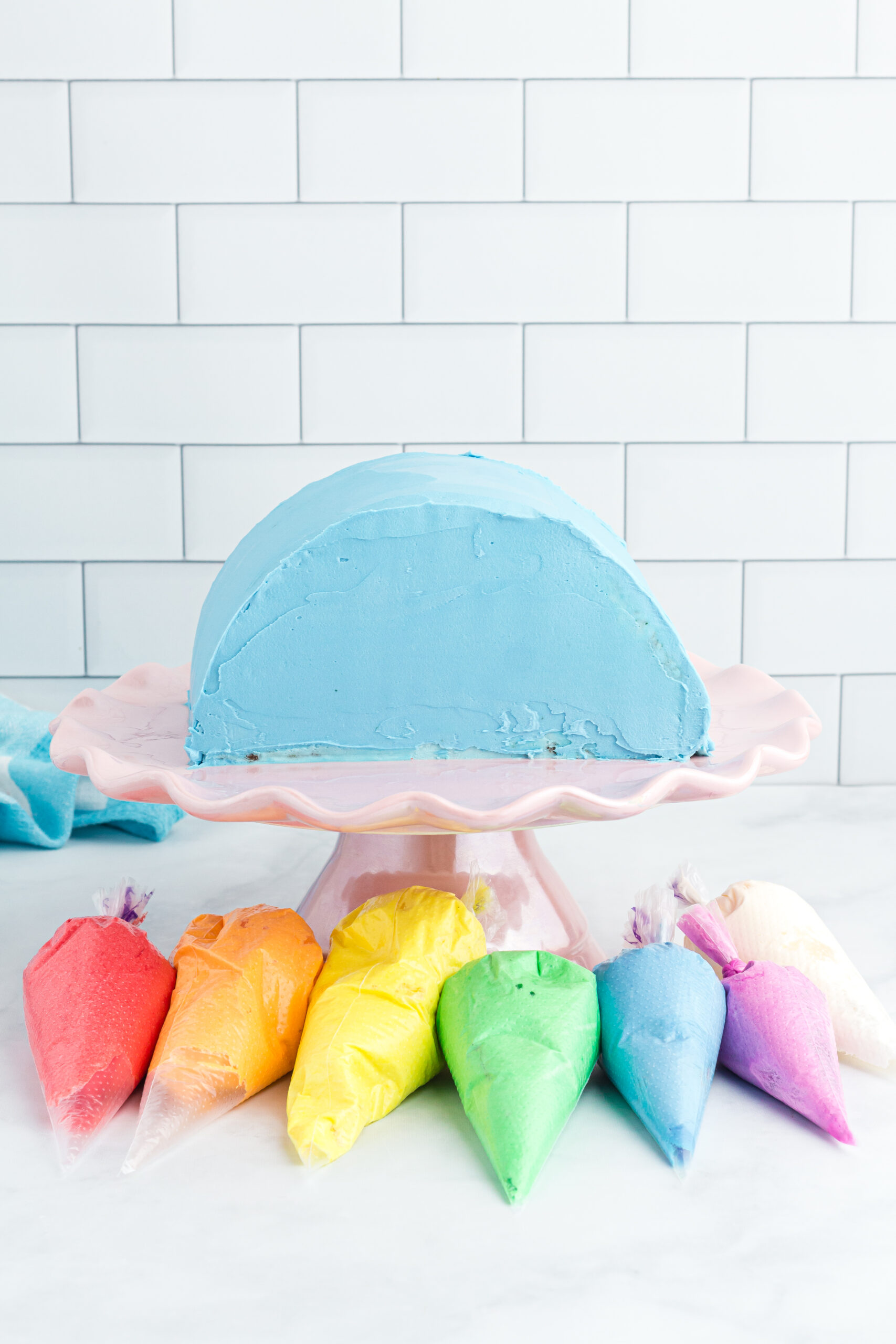 preparing to add rainbow colored frosting to blue frosted rainbow shaped cakes
