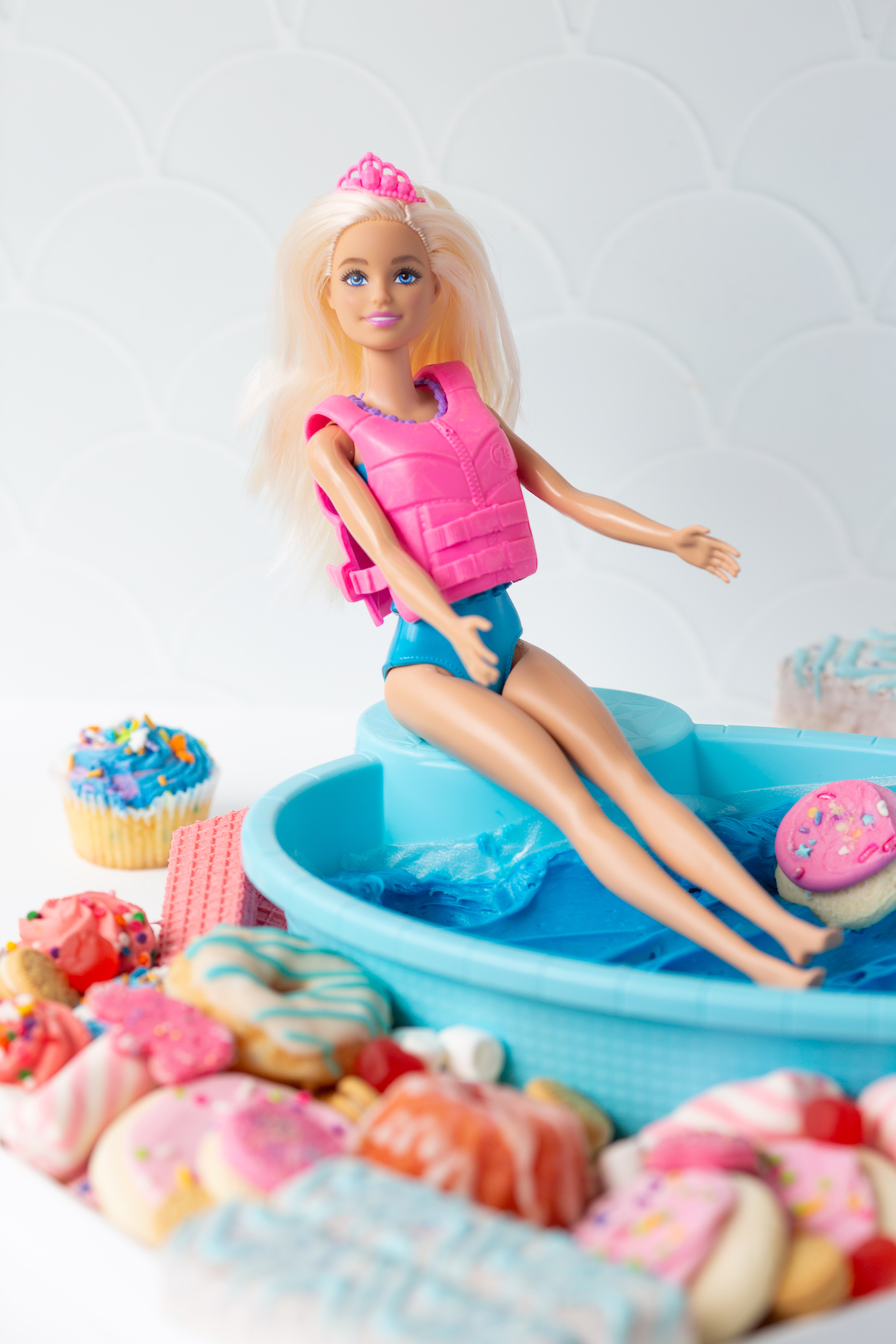 barbie sitting over a frosting filled pool on a dessert board