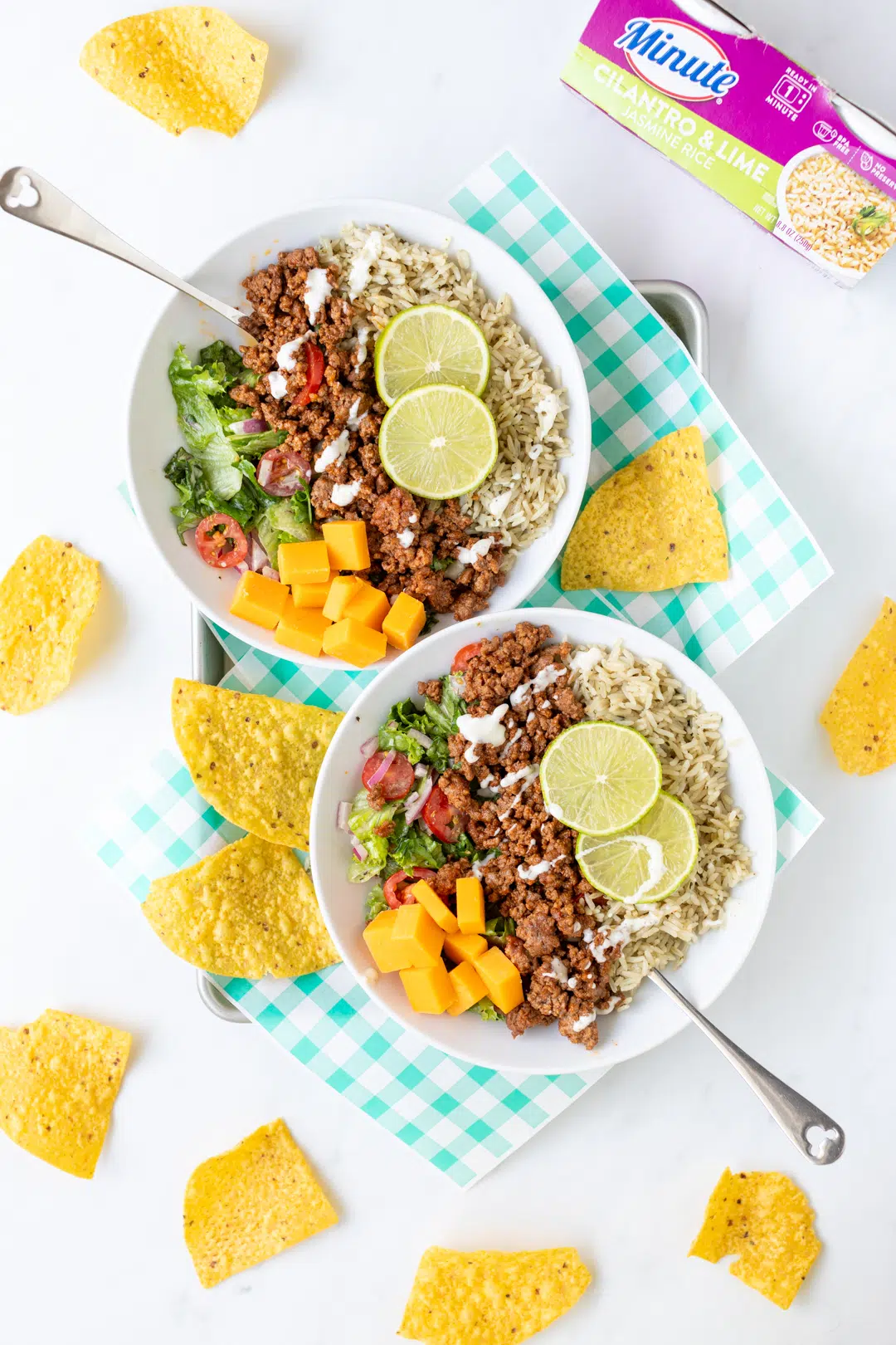 delicious rice bowls with seasoned beef, fresh salad ingredients, lime slices and chunked cheese.