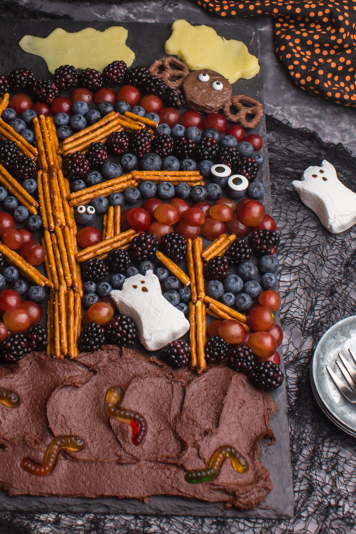 angled down view of spooky forest halloween treat board with fruit, pretzels and frosting