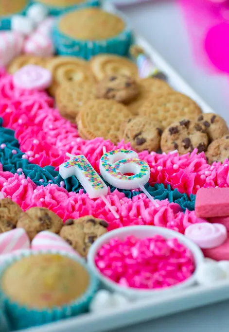angled down view of birthday buttercream board with cookies, sprinkles and birthday number candles in 16.