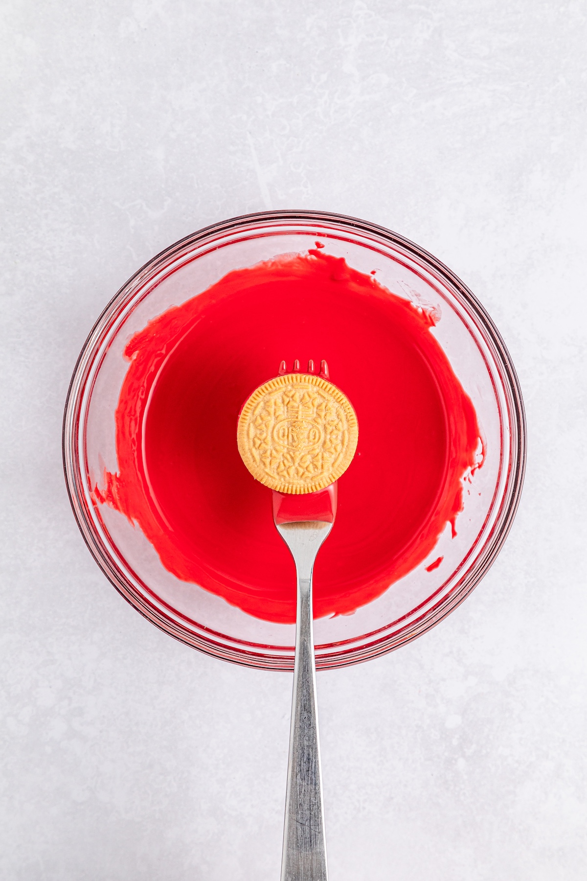 bowl of melted red chocolate with a golden Oreo on a fork over top