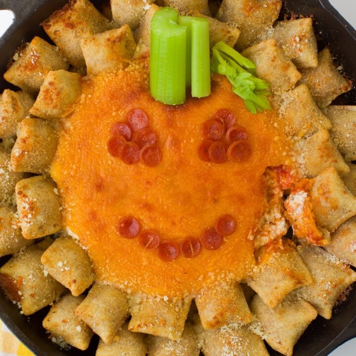 Jack-o'-lantern pizza dip in a skillet served with pizza rolls