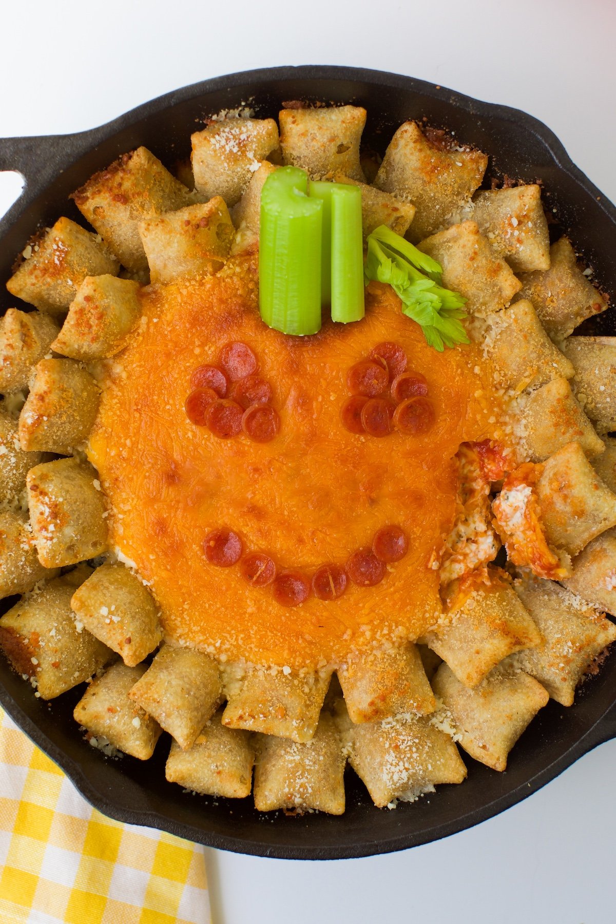 Jack-o'-lantern pizza dip in a skillet served with pizza rolls