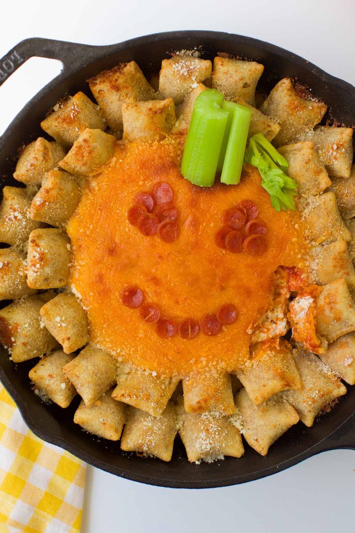 Jack-o'-lantern pizza dip topped with pepperoni and celery with pizza skillets.