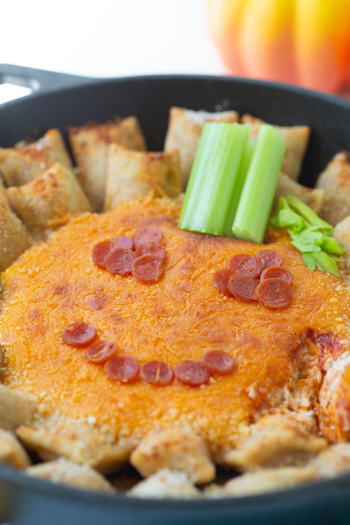 Angled view of skillet Jack-O'-Lantern Dip baked with pizza rolls.