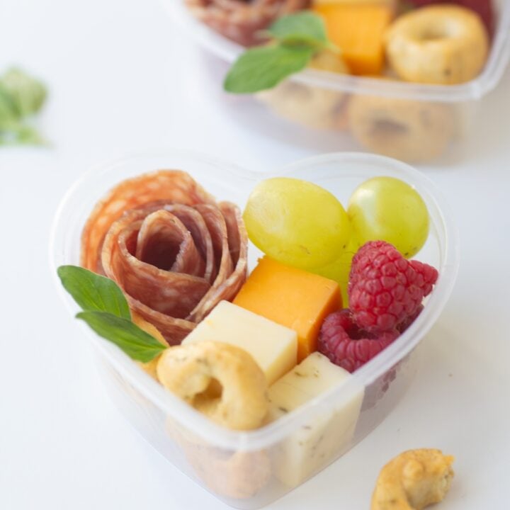 A close-up of the perfect Mini Heart Charcuterie Box stacked with succulent strawberries, creamy cheeses, and salami.