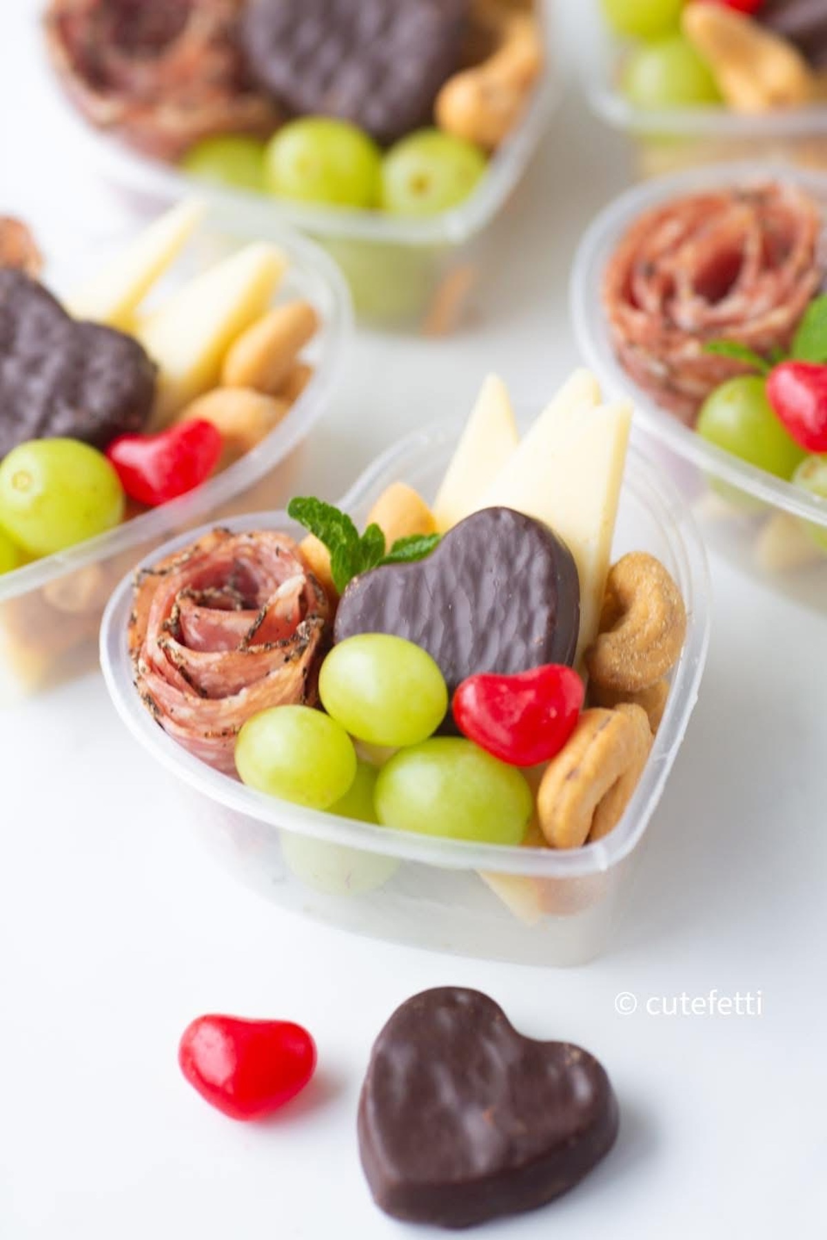 cute mini charcuterie heart container for valentine's day with fruit, salami, candy, chocolate and cashews.