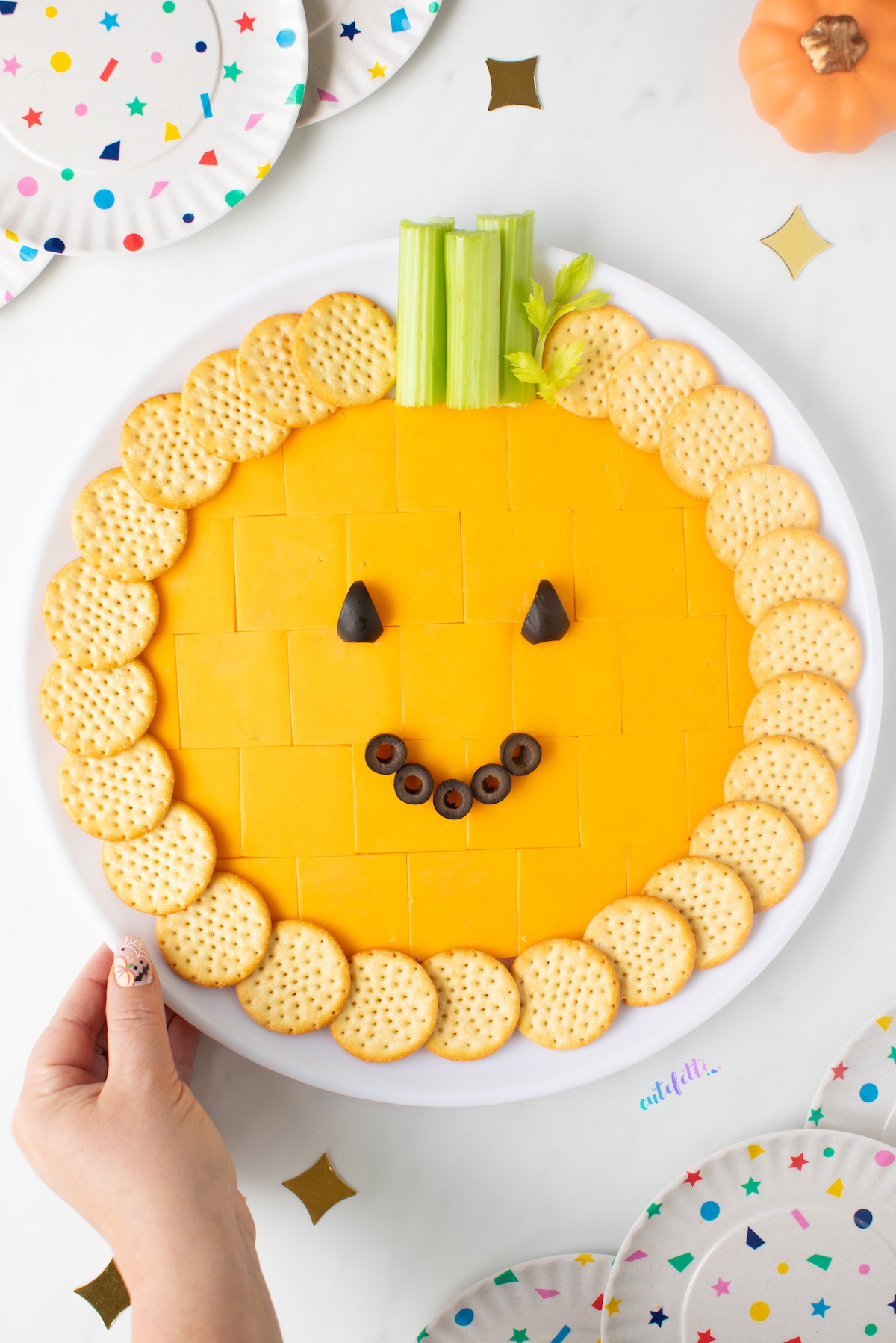 pumpkin cheese tray with cheddar cracker cuts, crackers, celery and black olives.
