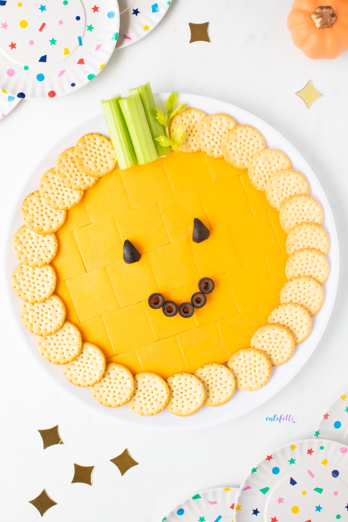 The pumpkin cheese tray is packed with cheddar cracker cuts, crunchy crackers, celery, and black olives.

