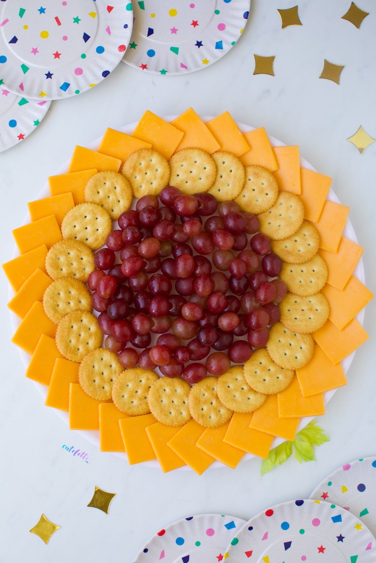 large sunflower cheese tray made with cheddar, crackers and red grapes. Celery leaves as an accent.