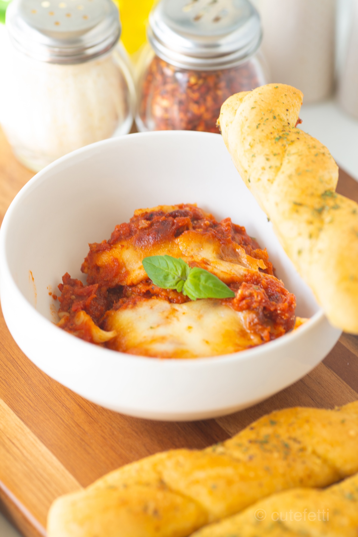 dish with lasagna topped with basil on top. served with breadsticks.